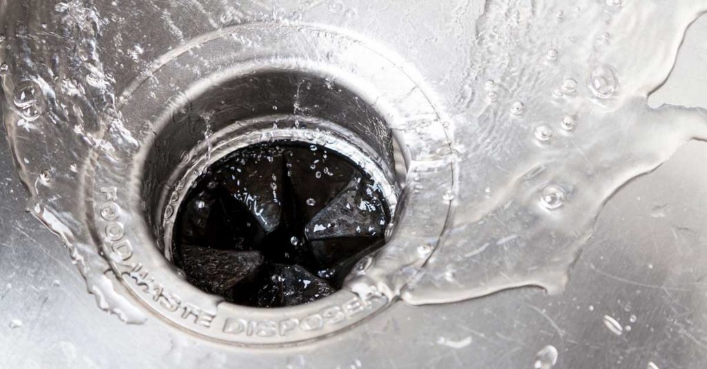 Closeup photo of water going down the drain in a kitchen sink with garbage disposal visible.
