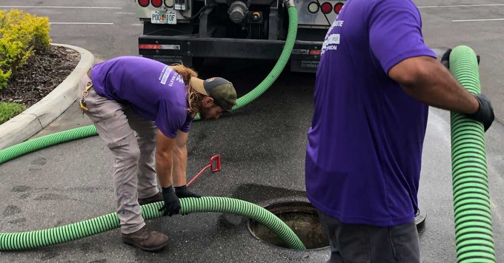 Photo of two ACE Septic & Waste employees holding green hoses going into a septic system hole.