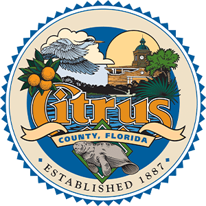 Logo emblem of Citrus County Florida showing a badge with an illustration of orange plant, cloud, sky, sun and a town hall building.