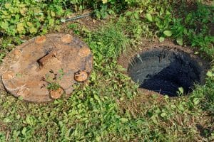 Photograph of an overhead view of green grass and sewer cesspool in a private house, open lid for inspection and maintenance.