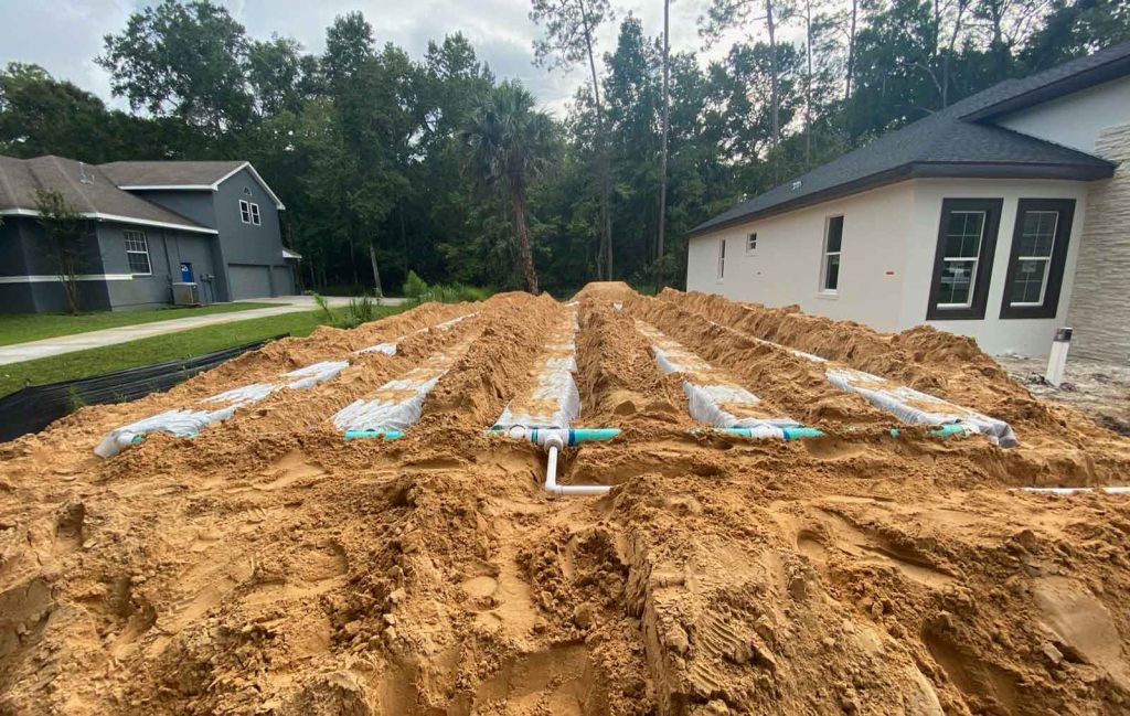 Photo of a Florida suburban neighborhood with red dirt and exposed new septic system installation next to a cream colored house.