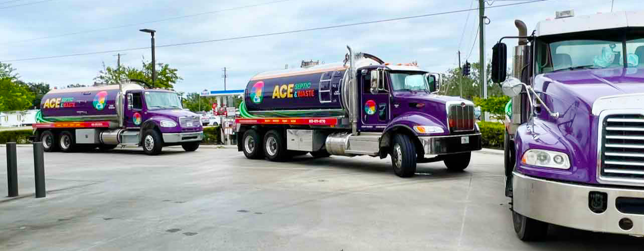 Photograph of a blue cloudy sky, trees, and pavement in a Florida neighborhood with 3 large purple septic pump trucks in a line, like a fleet.