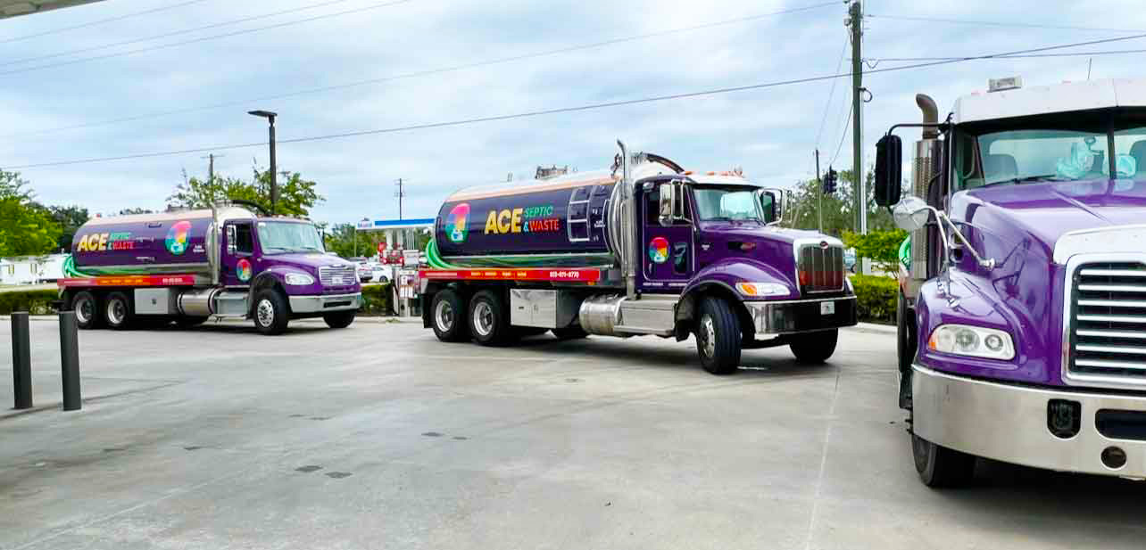 Photograph of a blue cloudy sky, trees, and pavement in a Florida neighborhood with 3 large purple septic pump trucks in a line, like a fleet.