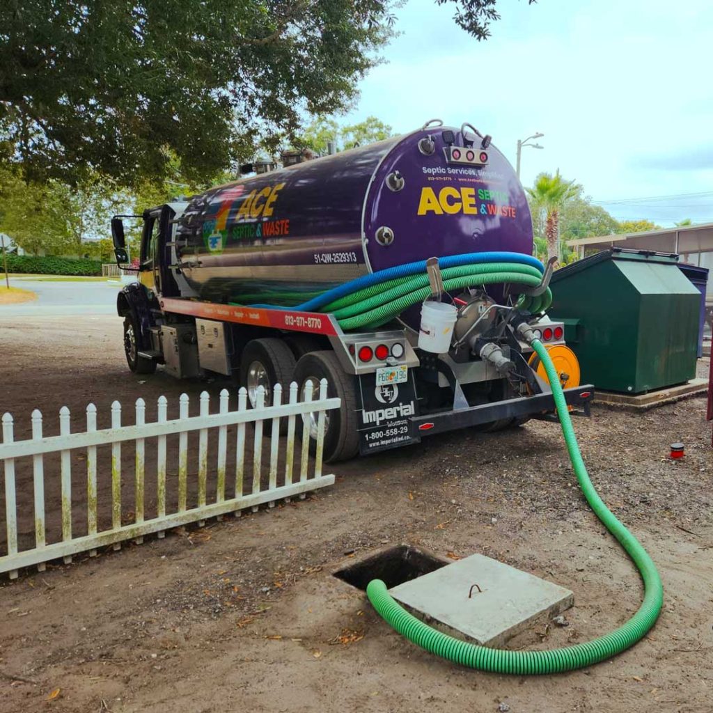 Photograph of a large purple septic pump truck that says ACE Septic & Waste, with a large green hose going into the ground.