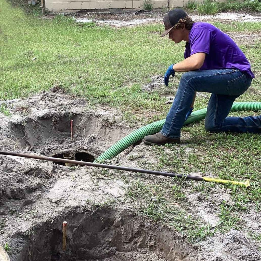 A person looking into a septic system with a large hose pumping out sewage.