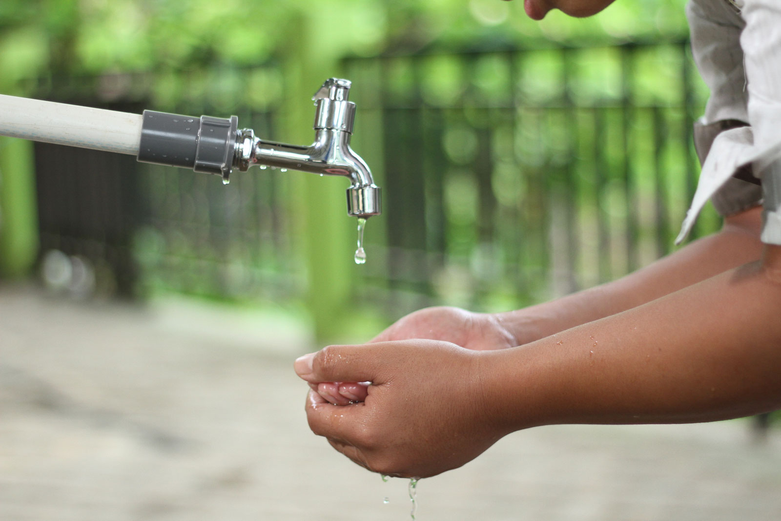 Photo of a hand in front of a faucet outdoors in a park, catching the water in order to drink.