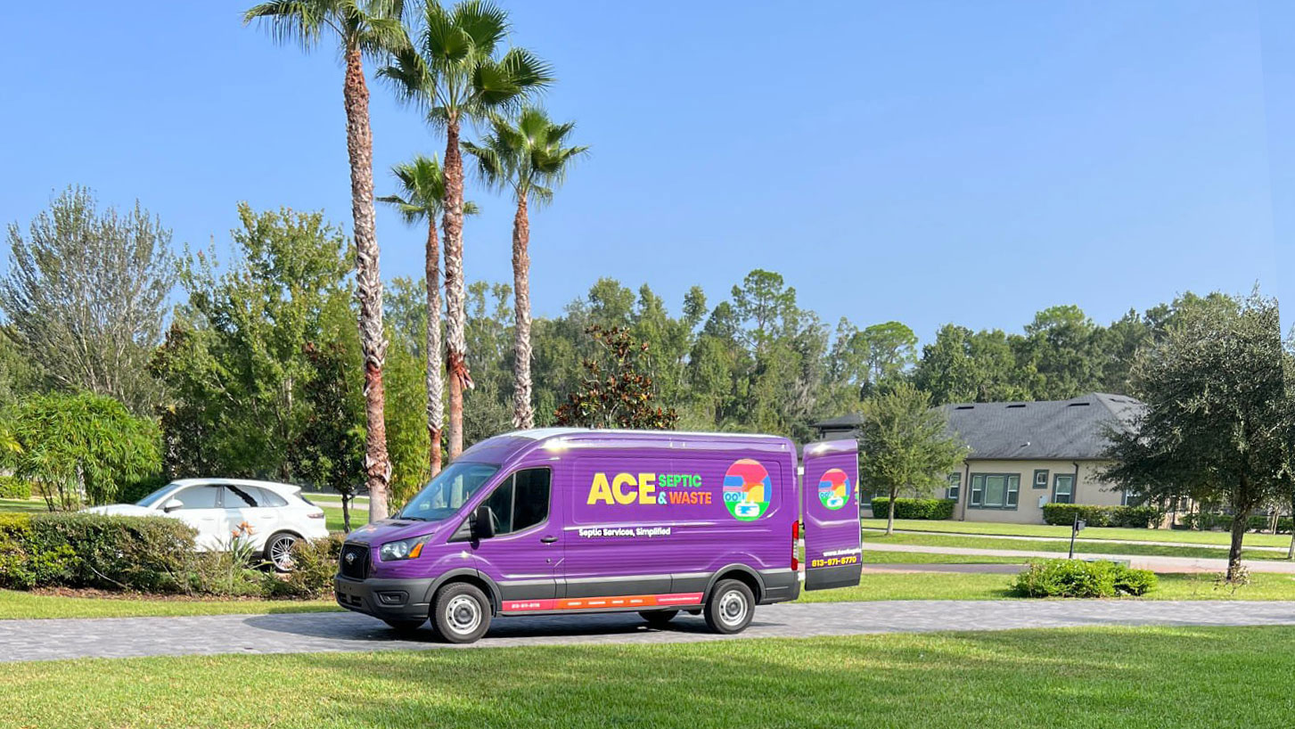 A purple cargo truck with the ACE Septic & Waste logo parked in the driveway with palm trees in the background.