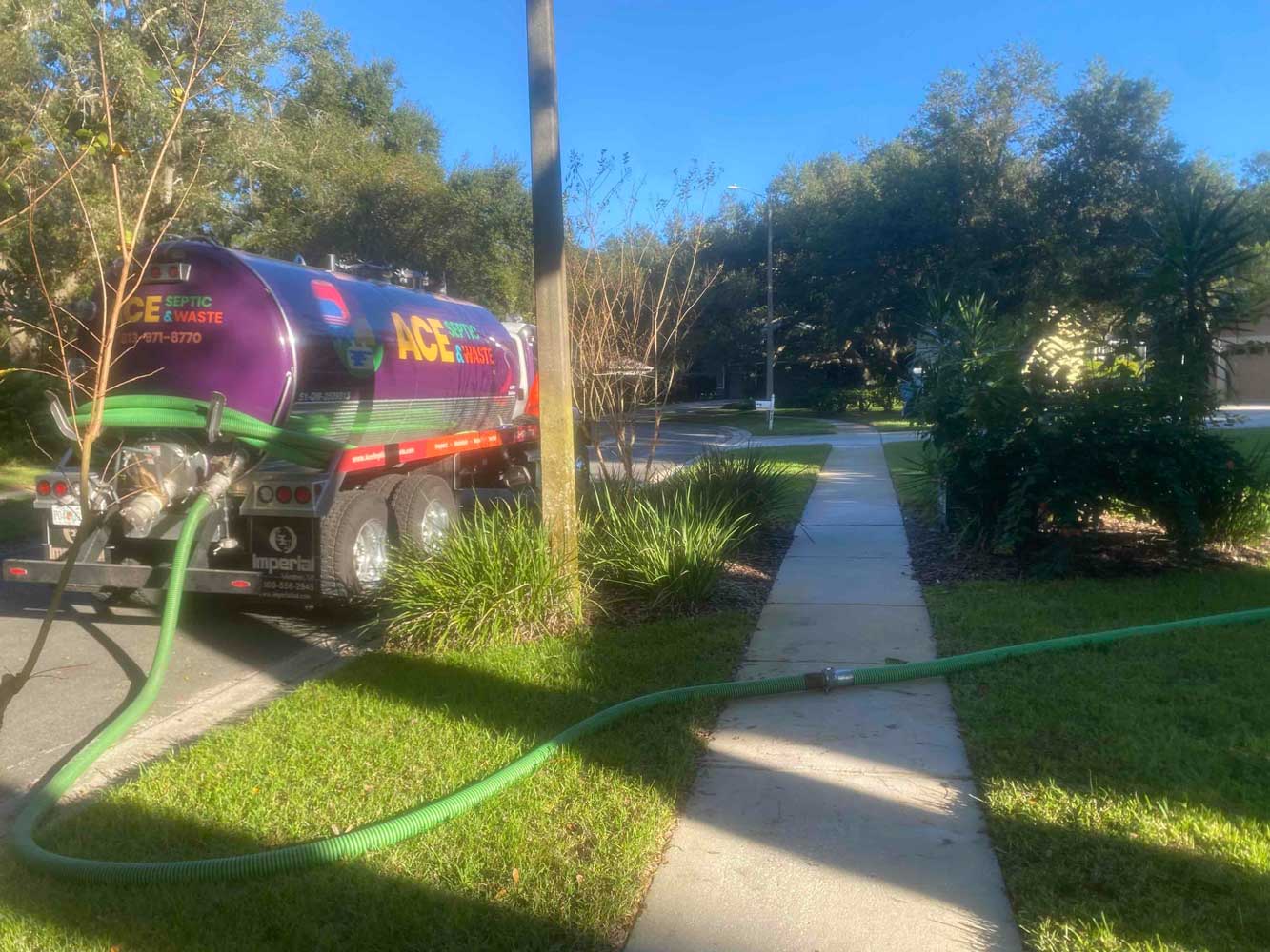 A septic truck with an extended hose across pavement leading towards a septic system.