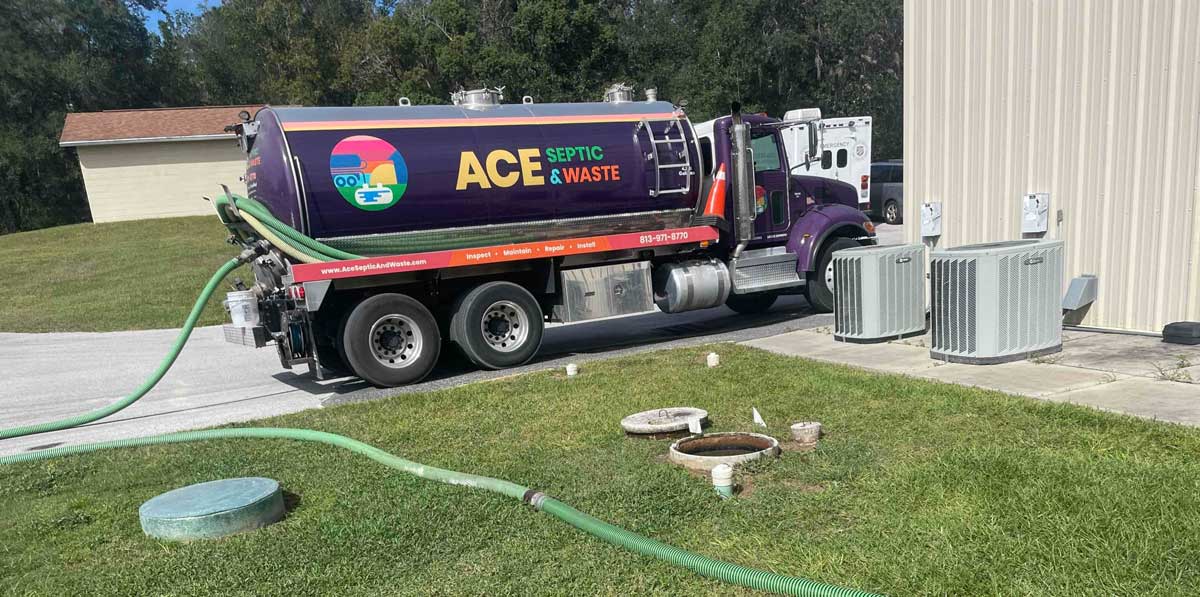 A photo of a septic truck with a colorful decal with the company name ACE Septic & Waste, that is pumping out a septic system
