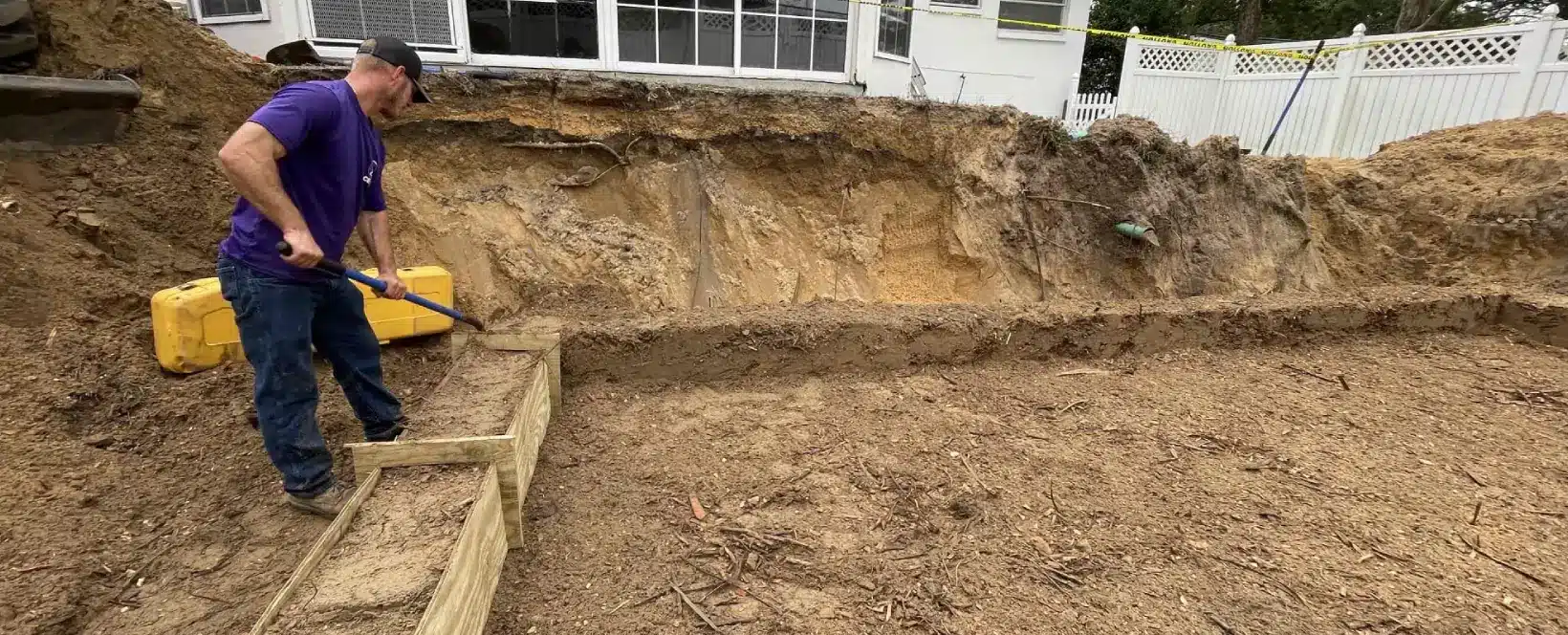 A worker smoothing dirt walls for a drain field installation.